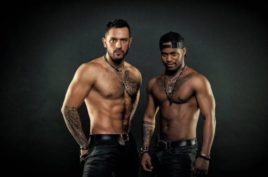 Formda ve seksi vücutlu erkekler. Yakışıklı gülüşlü, beyzbol şapkalı Afrikalı bir adam. Siyah arka planda kolları ve göğüsleri dövmeli sporcular, vücut bakımı konsepti. Sporcular yarışmaya hazırlanıyor