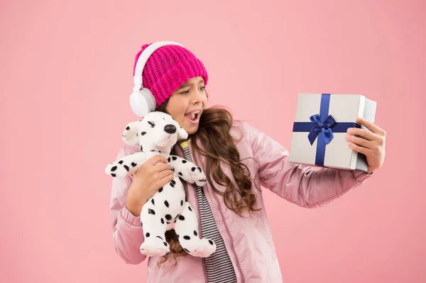 Happy childhood concept. Best gifts for teen girls. Stylish schoolgirl play with dog toy and hold gift box. Girl little fashionable cutie with headphones carry soft toy. Take favorite toy with you