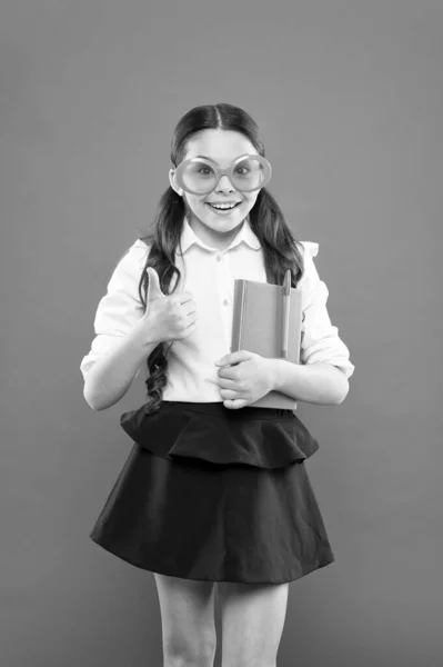 Erfolgskonzept. glückliches Schulmädchen in Uniform und Partybrille. Kleinkind mit Notizbuch. Literaturunterricht. Schreiben im Arbeitsbuch. Kinderliteratur. Informationen aus Buch beziehen — Stockfoto