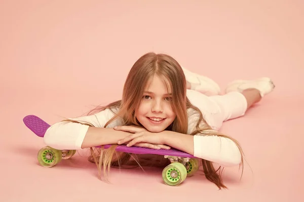 Chica de moda. Montar tablero de peniques y hacer trucos. A la chica le gusta andar en monopatín. Estilo de vida activo. Chica divirtiéndose con penny board fondo rosa. Niño adorable niño largo pelo adorar paseo penny board — Foto de Stock