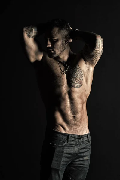 Deportista con seis paquetes y ab. El hombre tatuado muestra un sexy torso muscular. Culturista con bíceps y tríceps. Modelo de moda con tatuaje en jeans. Cuidado del cuerpo con fitness y deporte en filtro vintage — Foto de Stock