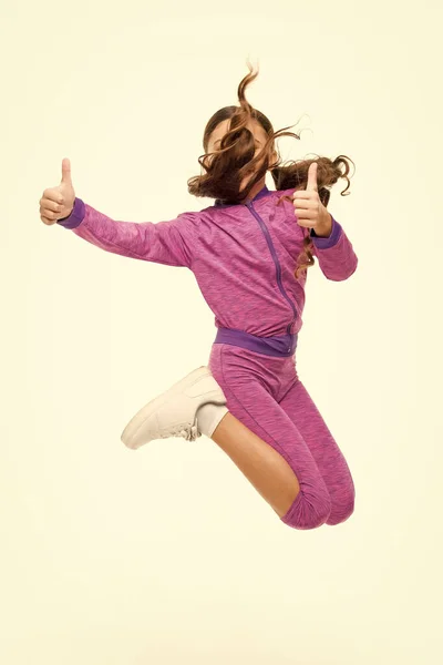 This child is active. Active little girl gesturing thumbs ups in motion isolated on white. Small child jumping in active sportswear. Fit and energetic kid. Getting more active and energetic — Stock Photo, Image
