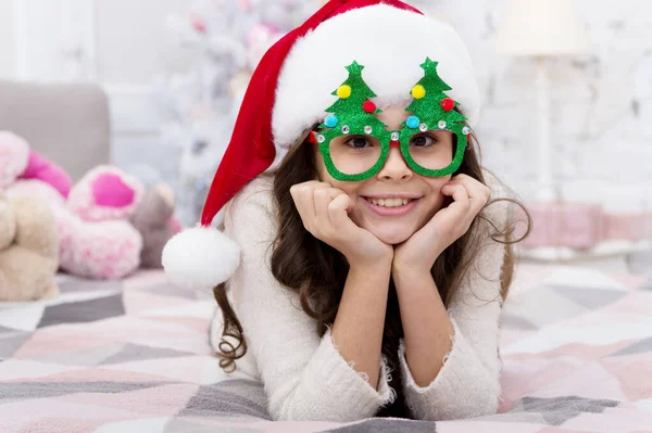 Happy new year. Wish list. Holidays atmosphere. Christmas spirit. New year holiday. Small child wear santa hat celebrate new year at home decorated interior background. Girl kid in bedroom with toys