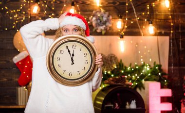 Kış partisi zamanı. Noel Baba şapkalı kadın klasik saat tutuyor. Kutlama zamanı. Yeni yıl geri sayımı. Beklenmedik bir şekilde yakında. Gece yarısı konsepti. Dilek tut. Mutlu noeller. Mucize zamanı. Birkaç dakika kaldı.