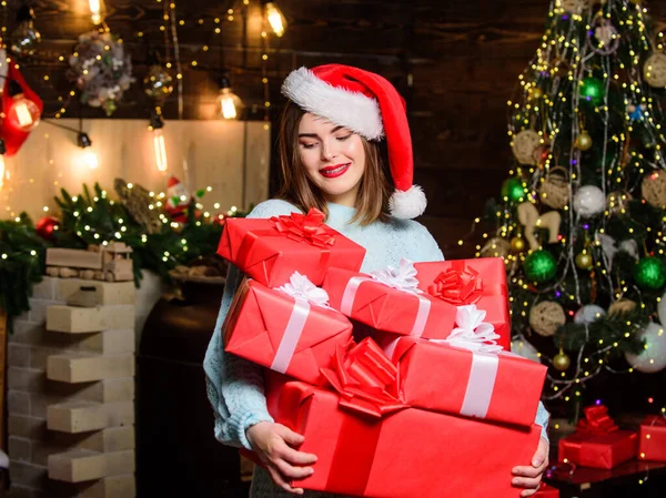 Vrouwe Kerstman viert thuis kerst. Meisje stijlvolle make-up rode lippen bevatten veel kerstcadeaus. Gezellige kerstsfeer. Vrouw kerstman hoed op kerstavond. Breng magie in iemand anders zijn leven. — Stockfoto