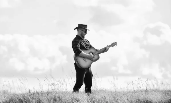 Inspirado músico country. Estilo country. Férias. Conceito de música country. Guitarrista country singer stand in field sky background. Canção para caminhadas. Unidos à natureza. Bonito homem com guitarra — Fotografia de Stock