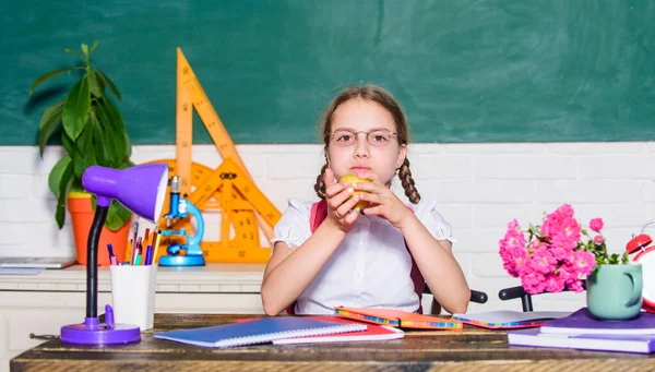 Μαθήτρια κάθεται γραφείο chalkboard φόντο. Κορίτσι μικρό παιδί τρώει μήλο σνακ. Σχολικές διακοπές. Χαλάρωσε ανάμεσα στα μαθήματα. Φόρτιση βιταμινών. Υγιεινός τρόπος ζωής Σχολική ζωή. Μαθητής στο σχολείο — Φωτογραφία Αρχείου