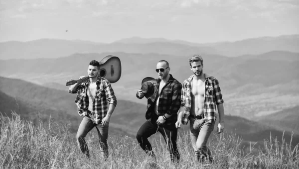 Group of young people in checkered shirts walking together on top of mountain. Tourists hiking concept. Hiking with friends. Friendly guys with guitar hiking on sunny day. Enjoying freedom together