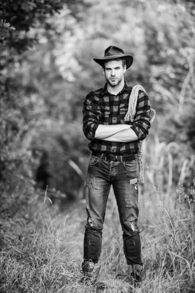 Man bär hatt hålla rep. Ranch ägare. "attle". Cowboy på landsbygden. Ranch yrken. Lasso-verktyget. Amerikansk Cowboy. Lasso bundet insvept. Västerländska livet. Man cowboy natur bakgrund. — Stockfoto