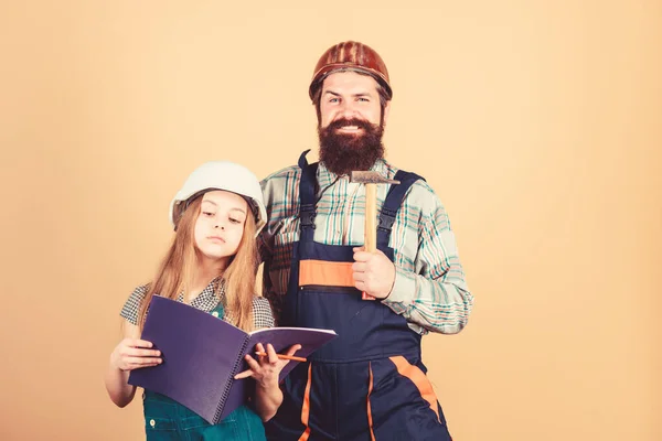 Padre barbudo hombre e hija casco casco uniforme renovando el hogar. Actividad de mejora del hogar. Niña planeando una renovación. Sala de renovación infantil. Casa de remodelación familiar. Pequeños padres ayudante — Foto de Stock