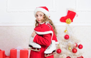 Noel ağacının yanındaki çocuk kış pateni tutuyor. Küçük kız Noel hediyesini beğendi. Gelmiş geçmiş en iyi hediye. Yeni yılın kutlu olsun. Artistik patinaj konsepti. Kış aktivitesi. Kış tatili konsepti