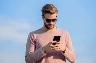 Hippi güneş gözlüğü takıyor cep telefonuyla gökyüzü arka planı tutuyor. Hippi akıllı telefon görüşmesi. Adam cep telefonu. İrtibatı koparmayalım. Mobil çağrı konsepti. Önemli bir cep telefonu sohbeti. Uygulama ve internet