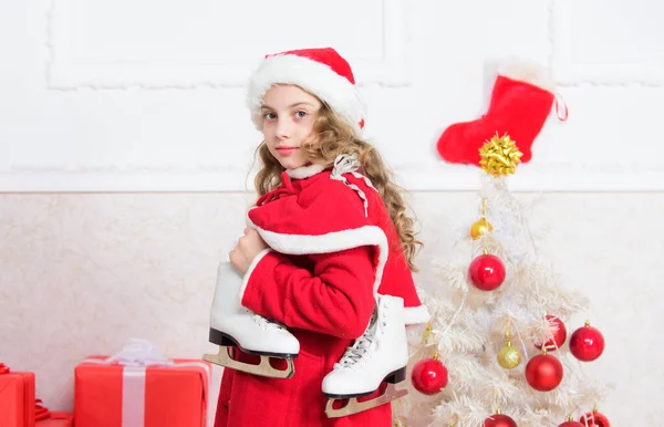 クリスマスツリーの近くの子供は冬のスケートを保持します。女の子はクリスマスの贈り物に満足した。最高の贈り物だ。冬休み明けましておめでとうございます。フィギュアスケートのコンセプト。冬のアクティビティ。冬のレジャーコンセプト — ストック写真
