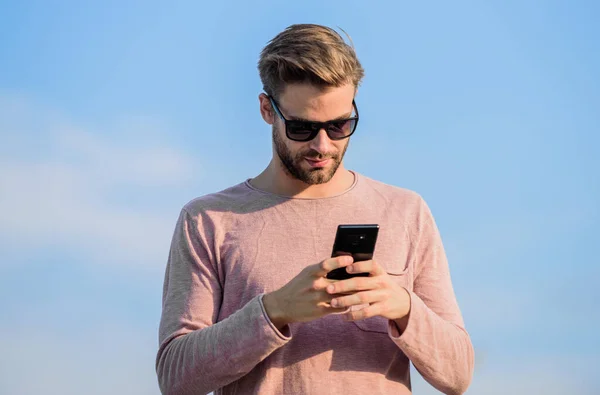Hipster wear sunglasses hold mobile phone sky background. Hipster smartphone call. Man mobile call. Stay in touch. Mobile call concept. Important mobile conversation. Application and internet