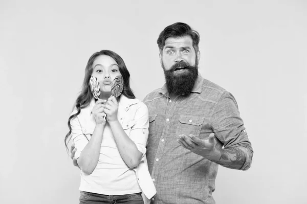 Sharing sweets with dearest people. Girl child and dad hold colorful lollipops. Sweet dessert. Bearded hipster good daddy for adorable daughter. Daughter and father eat sweet candies. Sweet childhood
