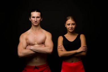 Herkes için spor. Seksi, uyumlu, siyah bir arka plan. Profesyonel spor takımı. Atletik erkek ve kadın kaslı kollarını kavuşturur. Formda kalmak için spor yapıyorum. Beden eğitimi ve spor