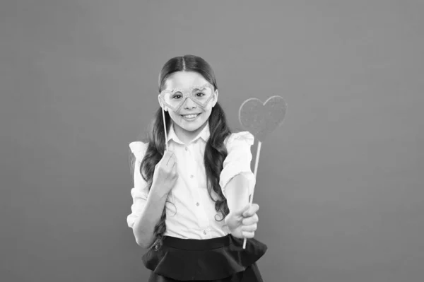 Hart liefde symbool. Kleine slimme schoolmeisje op oranje achtergrond. Kleine kind dragen oog bril slimme stijl. School Party concept. Kind slimme blik door Photo Booth Props Brillen. Valentines Day — Stockfoto