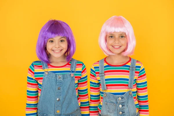 Moda moderna é criada para desfrutar. Meninas felizes usam perucas de cabelo moda fundo amarelo. Crianças pequenas sorriem em estilo casual. Moda chique. Salão de beleza e cabelo — Fotografia de Stock