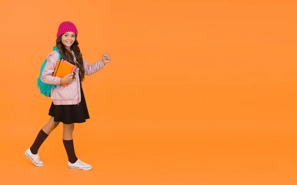 Visszatért az iskola. Boldog kisgyereket vissza az iskolába. A kislány narancssárga háttérrel jár iskolába. Vissza az osztályba. Szeptember 1. Üdvözöljük újra ősszel, másolás tér — Stock Fotó