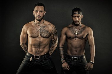 Sporcular fit ile karanlık kot giyen organları, sağlık ve vücut bakım kavramı. Dövmeli sandıkları ve kolları ile Afrika ve beyaz erkekler. Ciddi yüzü siyah arka plan üzerine izole olan erkekler
