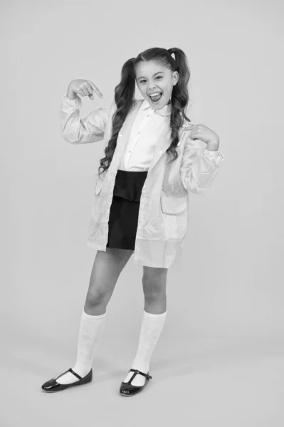 Soy guay. Niño pequeño y feliz señalando con los dedos sobre fondo amarillo. Pequeño escolar en el día de otoño. Niña pequeña de vuelta a la escuela con tiempo lluvioso. Adorable niño pequeño en verde raingear —  Fotos de Stock