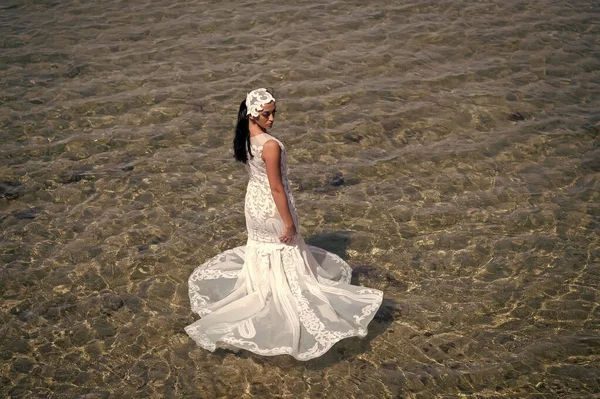 Matrimonio all'estero. Cerimonia nuziale in riva al mare. Sposa bianco abito da sposa stand in acqua di mare. Abito da sposa bagnato caldo giorno di sole. Sposa felice godere di vacanze estive sfondo oceano. Luna di miele in località balneare — Foto Stock