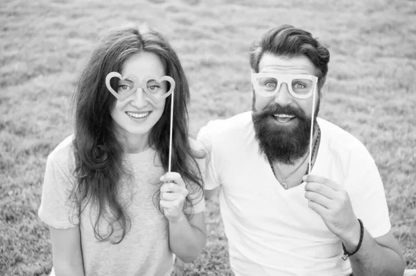 Fun Valentines props. Bearded man and sexy girl smiling with fancy party props on green grass. Funny couple holding heart shaped photobooth props on stick. Happy family celebrating with glasses props