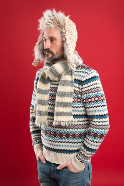 Erkek giyim konsepti. Moda koleksiyonu. Moda kıyafetleri. Örülmüş aksesuarlar. Soğuk kış koşulları. Şapka ve eşarp kırmızısı arka plan giyen yakışıklı sakallı adam. Kış modası. Isınıyorum. Sahte kürk