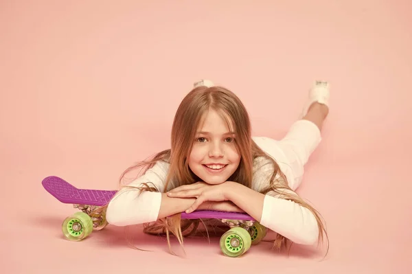 トレンディな女の子。子供愛らしい子供の長い髪はペニーボードに乗って崇拝。ペニーボードに乗って、トリックを行います。女の子はスケートボードに乗るのが好きです。アクティブなライフスタイル。ペニーボードピンクの背景を楽しんでいる女の子 — ストック写真