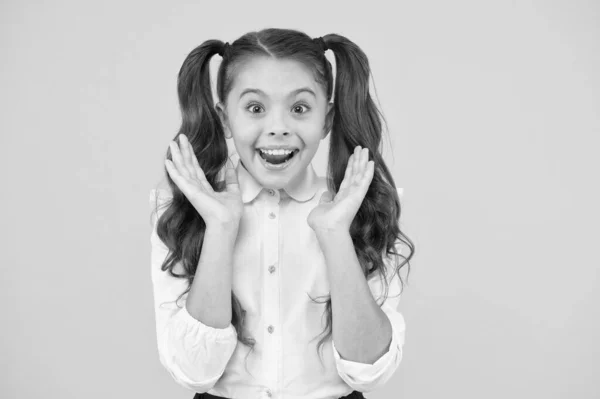 Volviendo a la escuela y luciendo encantado. niña sorprendida sonriendo sobre fondo amarillo. Niño pequeño con pelo largo y moreno con uniforme escolar formal. Chico feliz de vuelta a la escuela. La escuela es genial —  Fotos de Stock