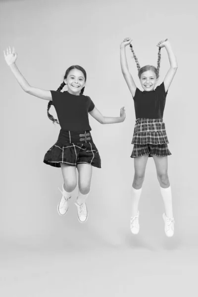 Comemore as férias. Férias escocesas. Crianças menina usar vestidos xadrez. Feriado nacional. Uniforme escolar. Estilo escocês. Junta-te à celebração. amigos alegres alunas saltando fundo amarelo — Fotografia de Stock