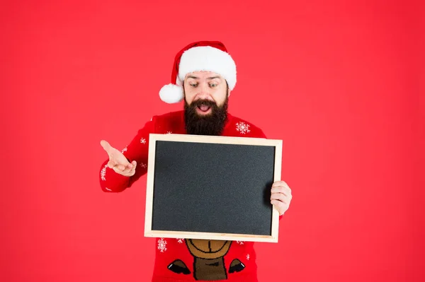 Inacreditável. Chapéu de Papai Noel com propaganda. Chalkboard para informação. Homem segurar espaço de cópia de quadro-negro em branco. Guy Pai Natal fundo vermelho. Anúncio de inverno. Evento de inverno. Férias de inverno — Fotografia de Stock