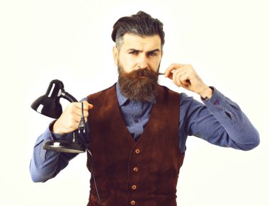 Sakallı adam elinde ciddi yüzüyle masa lambası tutuyor.