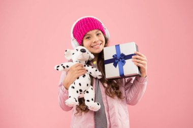 Kulaklıklı küçük, şık bir kız yumuşak oyuncak taşıyor. En sevdiğin oyuncağı yanına al. Mutlu çocukluk kavramı. Genç kızlar için en iyi hediyeler. Şık liseli kız köpek oyuncağıyla oynar ve hediye kutusunu tutar.