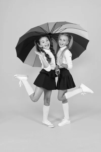 Moda de escuela primaria. Niños felices de la escuela con aspecto de moda sosteniendo paraguas colorido. Moda niñas pequeñas en uniformes formales sonriendo sobre fondo amarillo. Moda escolar para niños pequeños —  Fotos de Stock