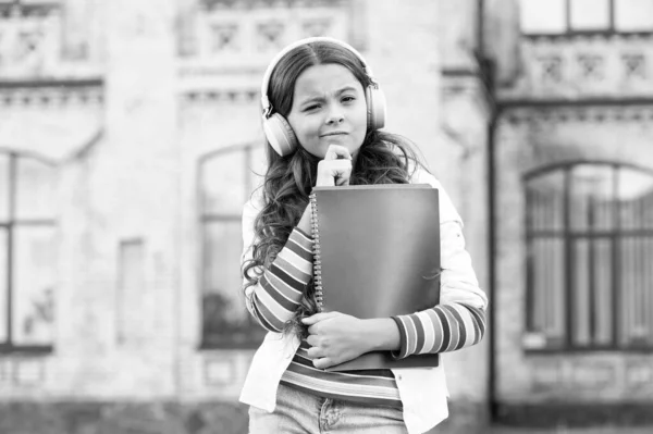 Rozwijanie skutecznych umiejętności słuchania. Poważna dziewczynka słuchająca lekcji audio w słuchawkach. Słodkie małe dziecko ćwiczy słuchanie zrozumienia. Rób notatki podczas słuchania, aby zachować słownictwo — Zdjęcie stockowe