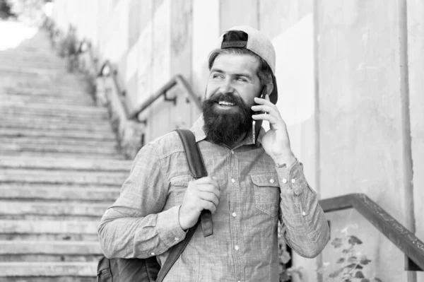 A boldogság utazik. Szakállas férfi beszél telefonon. boldog brutális ember séta utcán. Férfi fodrászellátás. brutális csípő és a hátizsák. túrakaland koncepció. városi stílusban. Érett csípő utazó — Stock Fotó