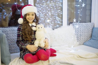 Kış bayramı. İyi tatiller. Evdeki çelenk ışıklarındaki küçük kız. Yeni yıl. Noel Baba. Küçük kız hediye aldı. Şimdiki Xmas. Kış anıları. Evdeki çocuk rahat pencere pervazında dinleniyor.