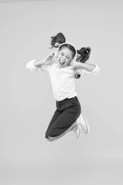 Música de felicidade. Criança pequena feliz pulando com felicidade no fundo amarelo. Menina pequena feliz gosta de ouvir música em fones de ouvido modernos. Frequência de felicidade. A felicidade está de volta à escola — Fotografia de Stock