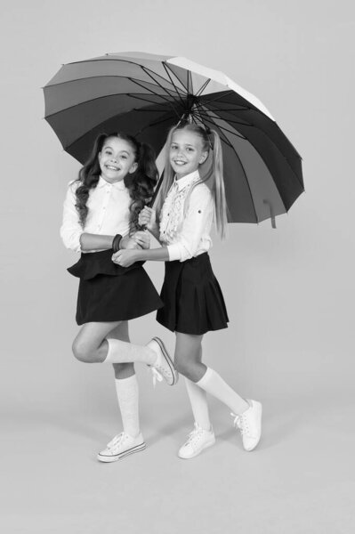 Autumn style. Happy small girls holding rainbow style umbrella on yellow background. Little children smiling in school style. Giving school fashion a sense of style