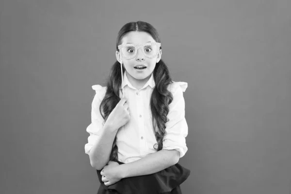 Ιδέα του σχολικού Κόμματος. Τι σημαίνει να είσαι έξυπνος. Μικρή έξυπνη μαθήτρια σε πορτοκαλί φόντο. Παιδικό έξυπνο βλέμμα μέσα από φωτογραφικό περίπτερο στηρίγματα γυαλιά. Μικρό παιδί φορώντας γυαλιά ματιών σε έξυπνο στυλ — Φωτογραφία Αρχείου
