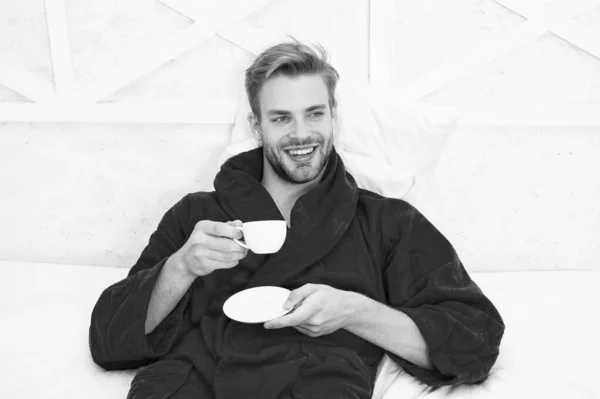 Kahvaltıda kahve içir. Yatakta kahve içen mutlu adam. Bornozlu sakallı adam elinde içki bardağını tutup gülümsüyor. Banyo spa sonra çay veya diğer sıcak içecek içme keyfini çıkarın — Stok fotoğraf