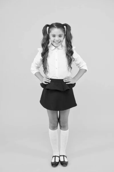 学校に戻るためのファッショントレンド。ファッションが黄色の背景に見える幸せな小学生。ファッションの制服で微笑む長い髪の小さな女の子。小さな学生のためのファッション — ストック写真