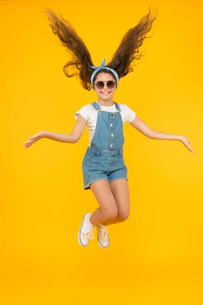 Cabelo comprido incrível. Menina pequena bonito com cabelo comprido pulando no fundo amarelo. Criança adorável desfrutar de longos cabelos morena. Melhor penteado para cabelos longos. Salão de beleza. Cabeleireiros salão — Fotografia de Stock