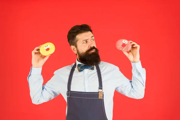 A comida sabe tão bem. Assadeira profissional com comida de sobremesa recém-assada no fundo vermelho. Homem barbudo segurando donuts comida caseira. Hipster assar comida doce — Fotografia de Stock