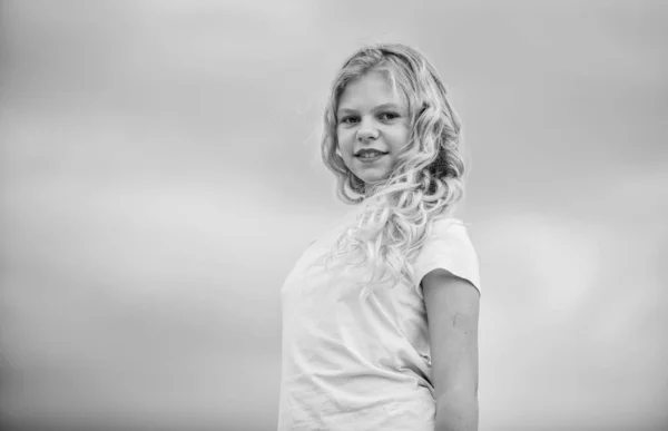 Services de salon de coiffure. Petite fille avec de longs cheveux bouclés fond ciel. Empêcher les pointes fourchues. Fille aux cheveux bouclés naturels sains. Coiffures bouclées et magnifiques. Procédure beauté. Adorable enfant — Photo