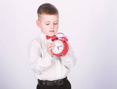 Çalar saati ayarlayın. Küçük çocuk kırmızı saati tutuyor. Zamanı oldu. Program ve zamanlama. Sabah rutini. Çalar saati olan bir öğrenci. Çocuk sevimli çocuk beyaz gömlek kırmızı papyon. Öz disiplini geliştirin