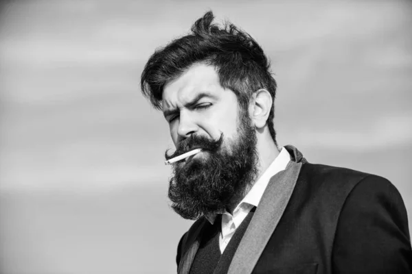 La vérité sur le plaisir de fumer et la dépendance à la nicotine. Hipster barbu fumant cigarette fond bleu ciel. Guy avec cigarette profiter de l'influence de la nicotine. Homme avec barbe et moustache tenir cigarette — Photo