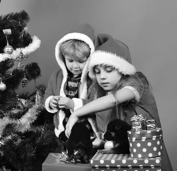 Bambini con volti curiosi disfare i regali su sfondo rosso. — Foto Stock