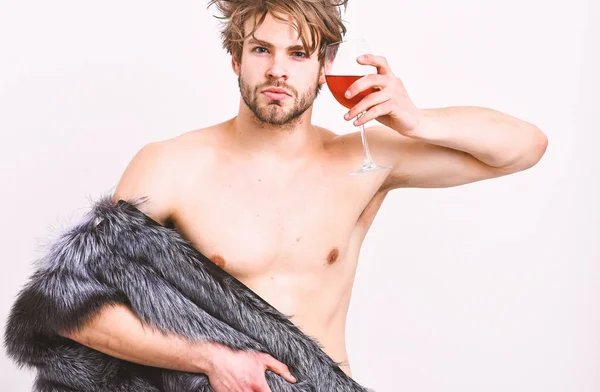 Chico atractivo rico posando abrigo de piel en cuerpo desnudo. Atleta rico disfrutar de su vida. Riqueza y concepto de lujo. Sexy soñoliento rico macho tousled pelo beber vino aislado en blanco. Moda y pathos — Foto de Stock